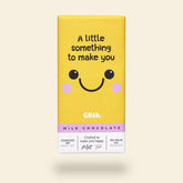 A yellow chocolate bar packaging with a smiling face and the text 'A little something to make you' on top. The brand 'GNAW' is visible at the bottom with the product description 'Milk Chocolate' and additional text indicating compostable packaging.